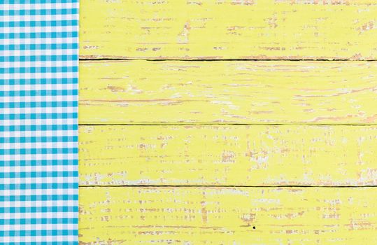 Blue checked tablecloth on rustic colored wooden table background, top view