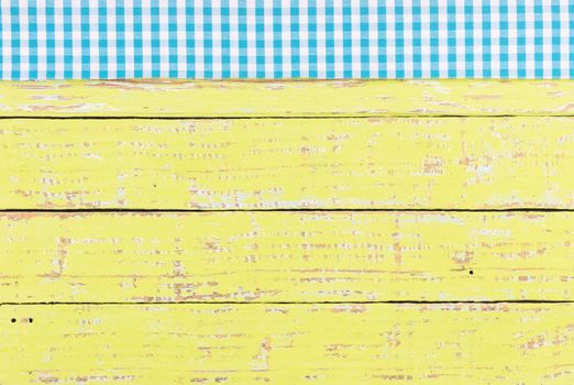 Rustic yellow wooden table surface with blue checkered cloth, top view