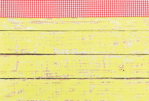 Rustic yellow wooden table surface with red checkered cloth, top view