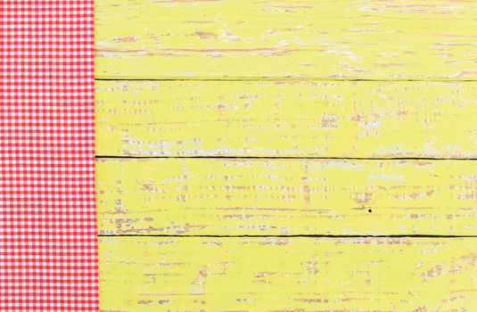Red checked tablecloth on rustic colored wooden table background, top view