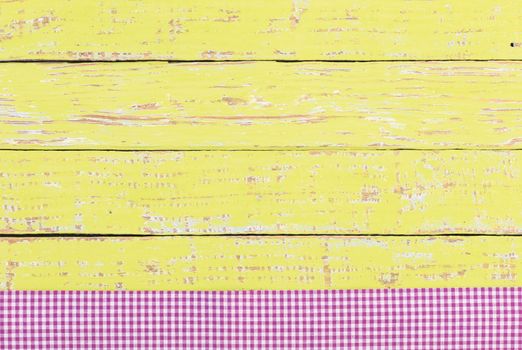 Rustic yellow wooden table surface with purple checkered cloth, top view