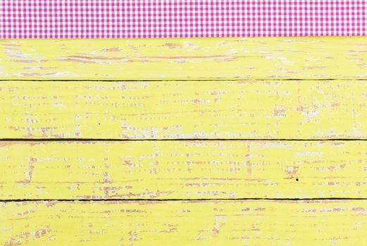 Rustic yellow wooden table surface with purple checkered cloth, top view