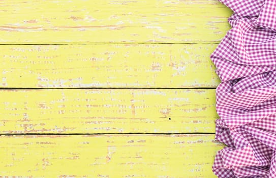 Yellow wooden table surface with rustic purple checkered cloth, top view