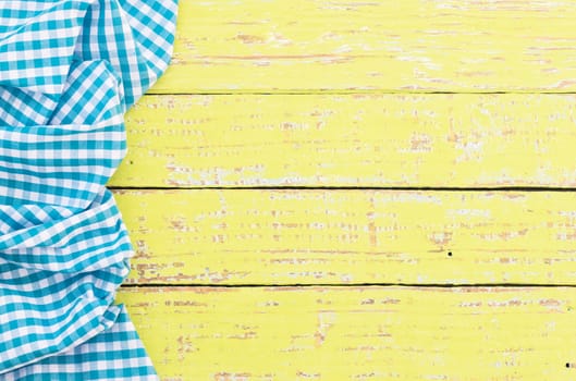 Yellow wooden table surface with rustic blue checkered cloth, top view