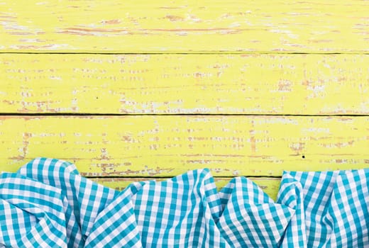 Yellow wooden table surface with rustic blue checkered cloth, top view