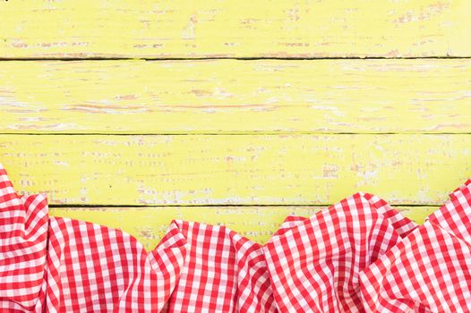 Rustic yellow wooden table surface with red checkered cloth, top view