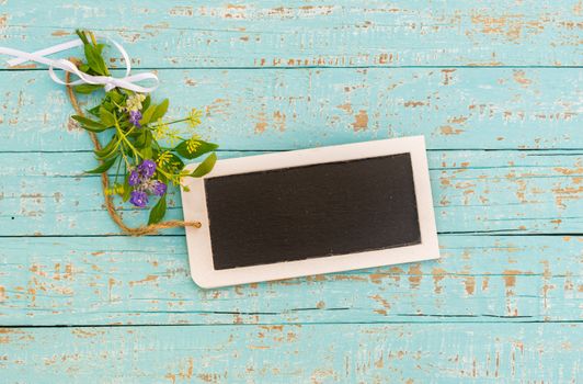 Flowers with small empty blackboard on blue wood background