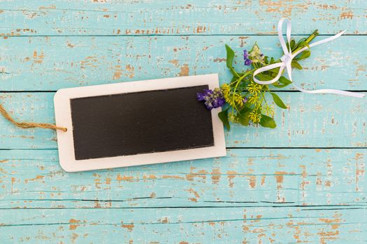 Bunch of flowers with small empty blackboard on blue wood background