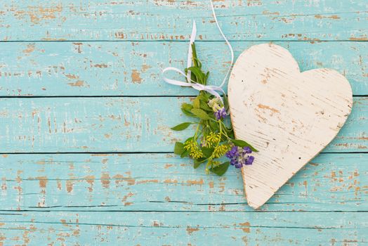 Turquoise background with white wooden heart and bunch of flowers with copy space