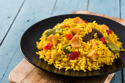 Fried rice with chicken and vegetables on black plate on blue wooden table