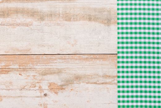 Green checked tablecloth on rustic wooden table background, top view