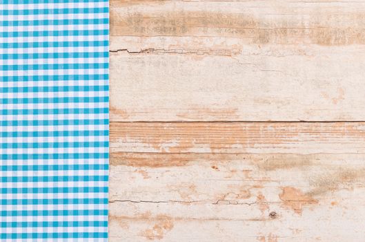 Blue checked tablecloth on rustic wooden table background, top view