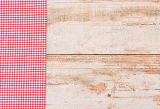 Red checked tablecloth on rustic wooden table background, top view