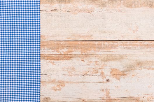 Blue checked tablecloth on rustic wooden table background, top view
