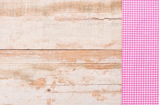 Pink checked tablecloth on rustic wooden table background, top view