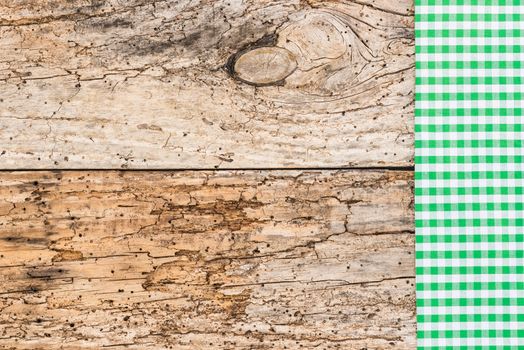 Green checked tablecloth on rustic wooden table background, top view