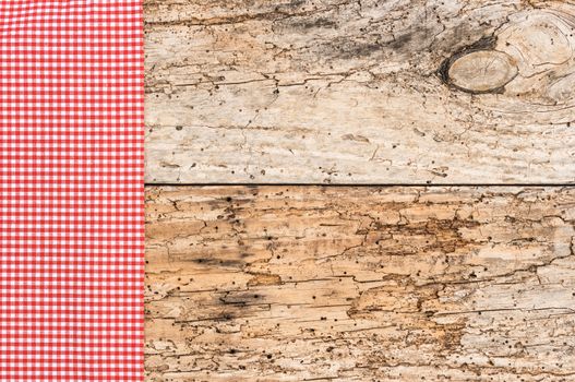 Red checked tablecloth on rustic old wooden table background, top view