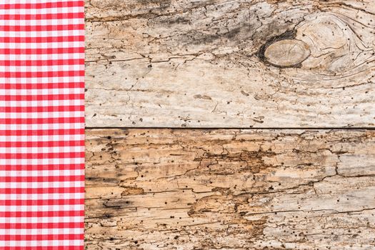 Red checked tablecloth on rustic wooden table background, top view