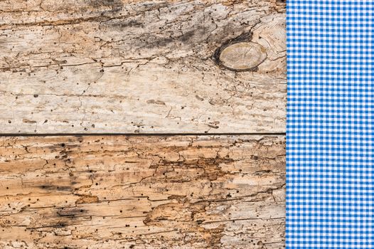 Blue checked tablecloth on rustic wooden table background, top view