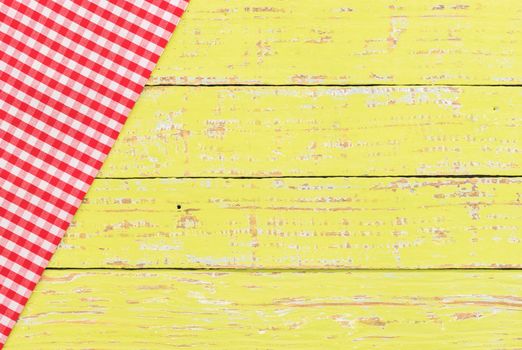 Red checkered tablecloth on rustic yellow wooden table background