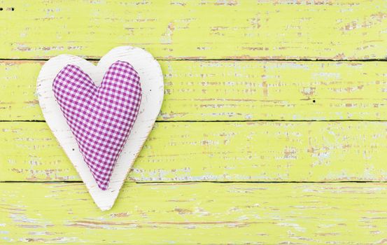 Rustic fabric heart on yellow wood background with copy space