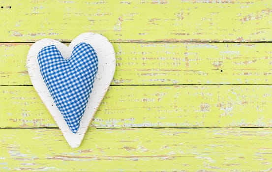 Blue fabric heart on light green wooden background with copy space