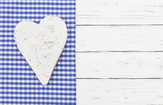 Rustic white heart on blue checked textile and white wooden background with copy space