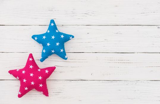 Blue and pink fabric stars on white wooden background with copy space