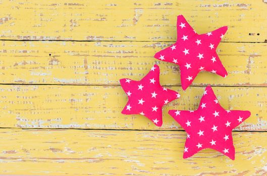 Red fabric stars on yellow wooden background with copy space
