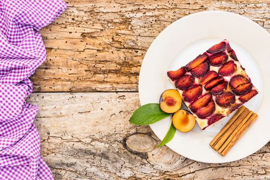 Delicious piece of cake with fresh plums and cinnamon on rustic wooden table