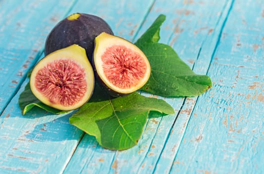 Fresh fig fruits with green leaves, close-up on blue wooden background