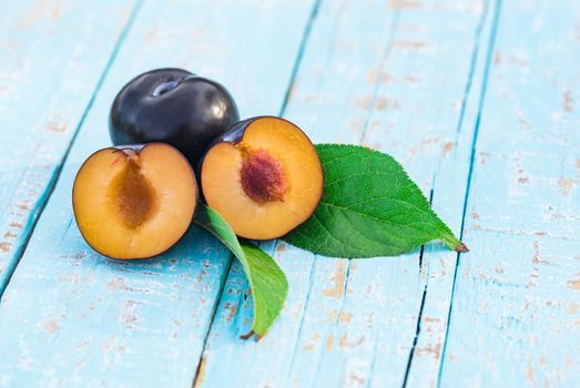 Sliced juicy plum with leaves on blue wooden table backtround