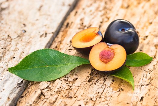 Sliced juicy plum with leaves on rustic wooden table backtround