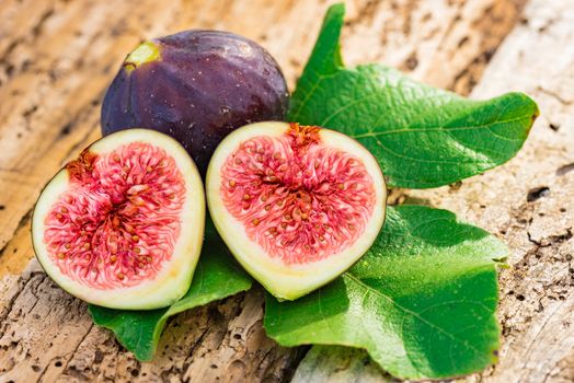 Close-up of fresh figs with green leaves on wooden table background