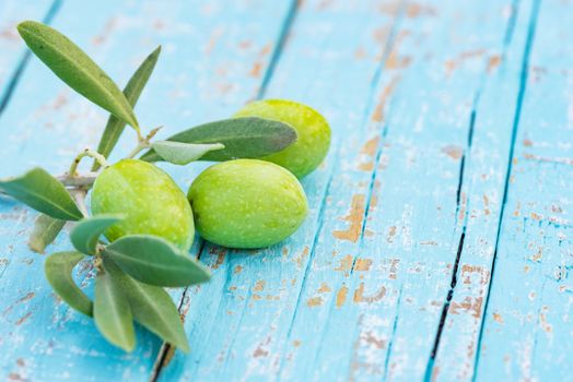 Close-up of fresh green olives with leaves on turquoise wooden table background