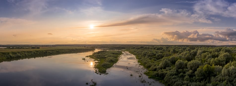 Aerial view to sunset on the river at summer evening with clouds and trees. Water reflection of a sky.