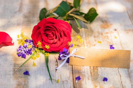 Beautiful red rose flower and blank label on rustic wooden table