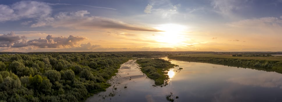 Aerial view to sunset on the river at summer evening with clouds and trees. Water reflection of a sky.