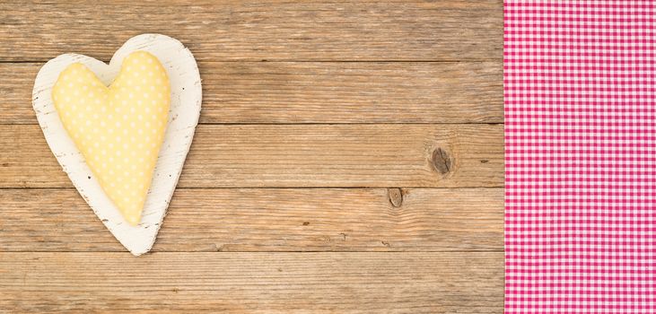 Yellow heart on wooden background with pink fabric border and copy space 