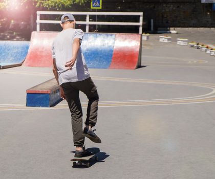 A teenage boy trains to ride a skateboard in a skate Park, a view from the back.