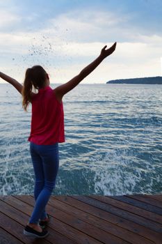 girl on a wooden pier with arms raised looks at the stormy sea