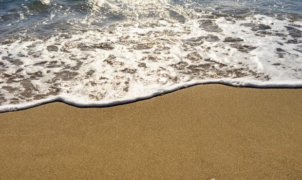 Soft wave of ocean water on golden sandy beach background