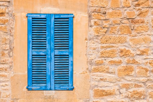 Detail view of blue window shutter with rustic stone wall background