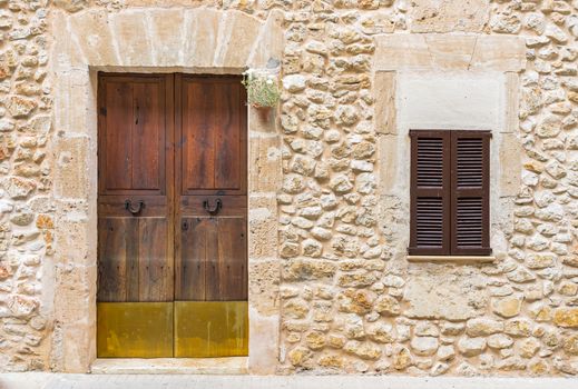 Rustic mediterranean house with stone wall, wooden front door and closed window shutters