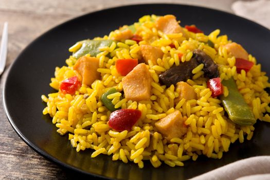 Fried rice with chicken and vegetables on black plate on wooden table