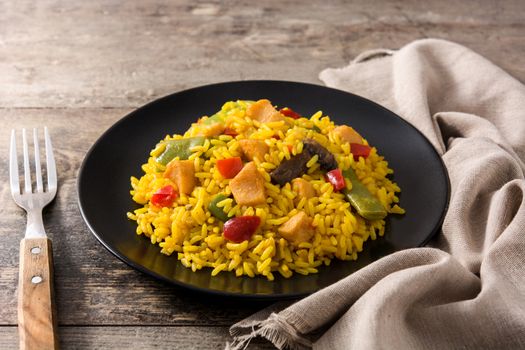 Fried rice with chicken and vegetables on black plate on wooden table