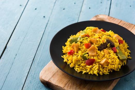 Fried rice with chicken and vegetables on black plate on blue wooden table