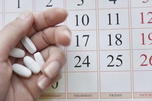selective focus at pills and calendar with blurry hand. schedu;ed treatment concept