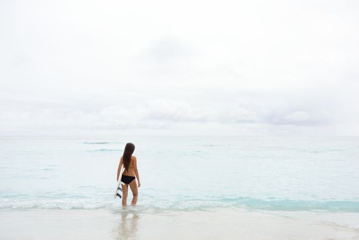 Surfer girl going surfing looking at ocean beach. Female bikini woman heading for waves with surfboard having fun living healthy active lifestyle. Water sports with model.