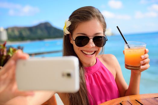 Selfie woman taking self portrait at beach bar during holidays. Young Asian adult holding smartphone camera to take a picture of herself during her summer vacations in Waikiki, Honolulu, Hawaii, USA.